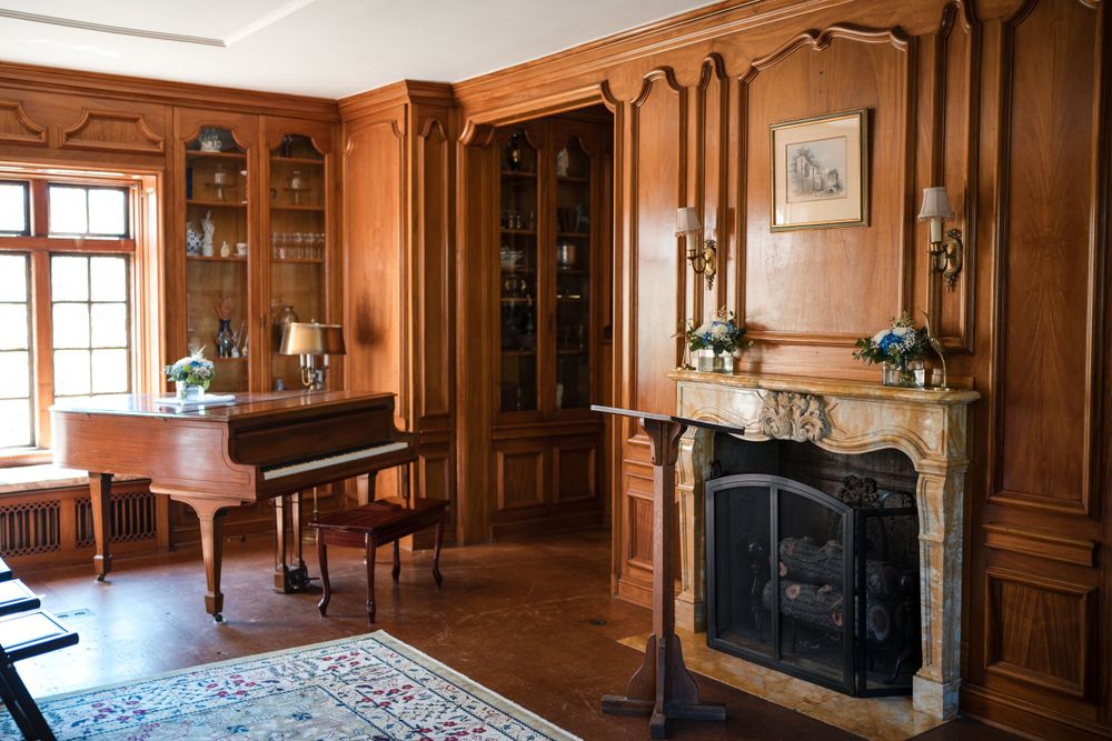 Elegant wood-paneled study with fireplace, built-in bookshelves and antique piano.