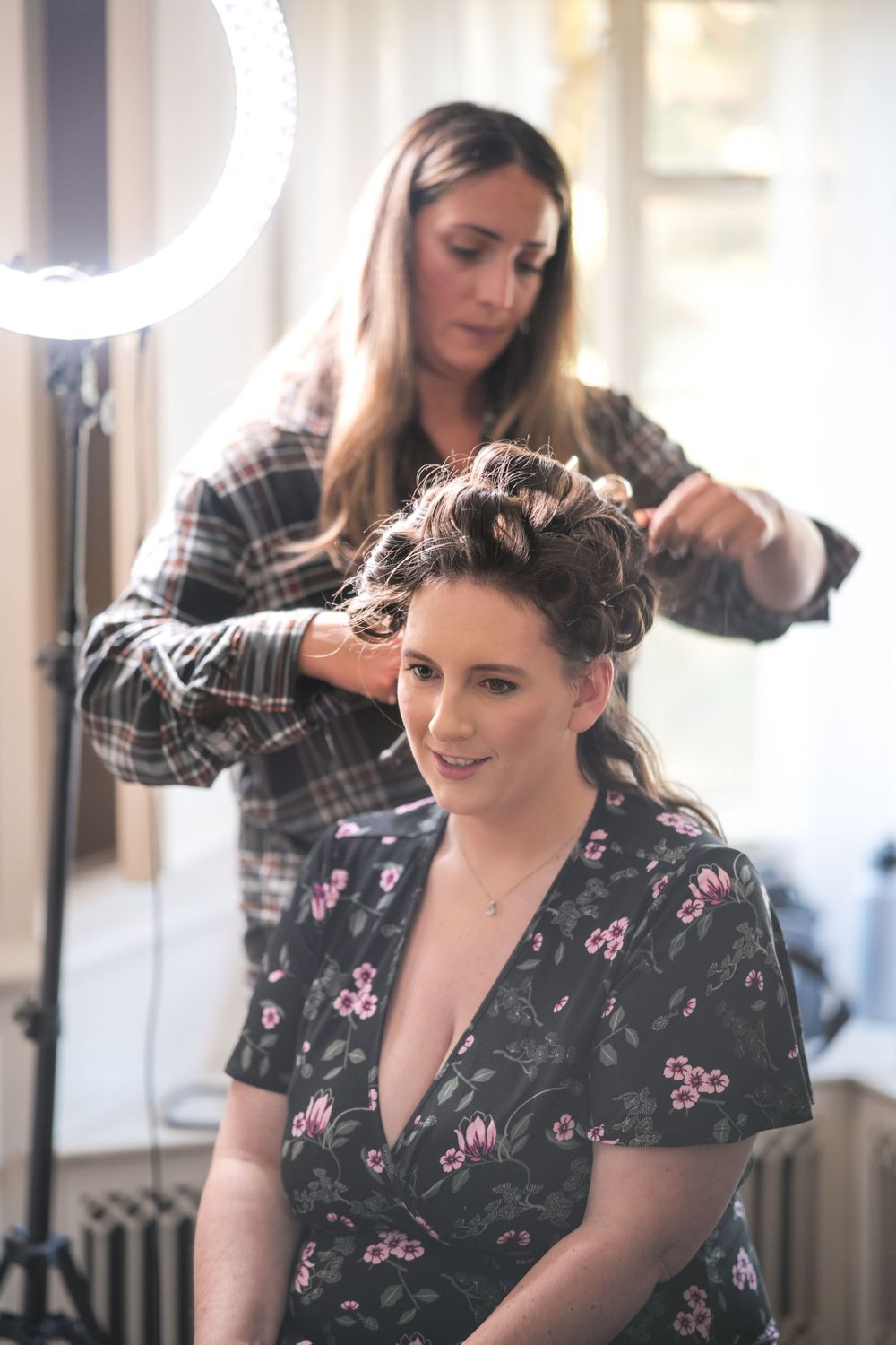 A hairstylist works on styling someone's hair in a well-lit room.