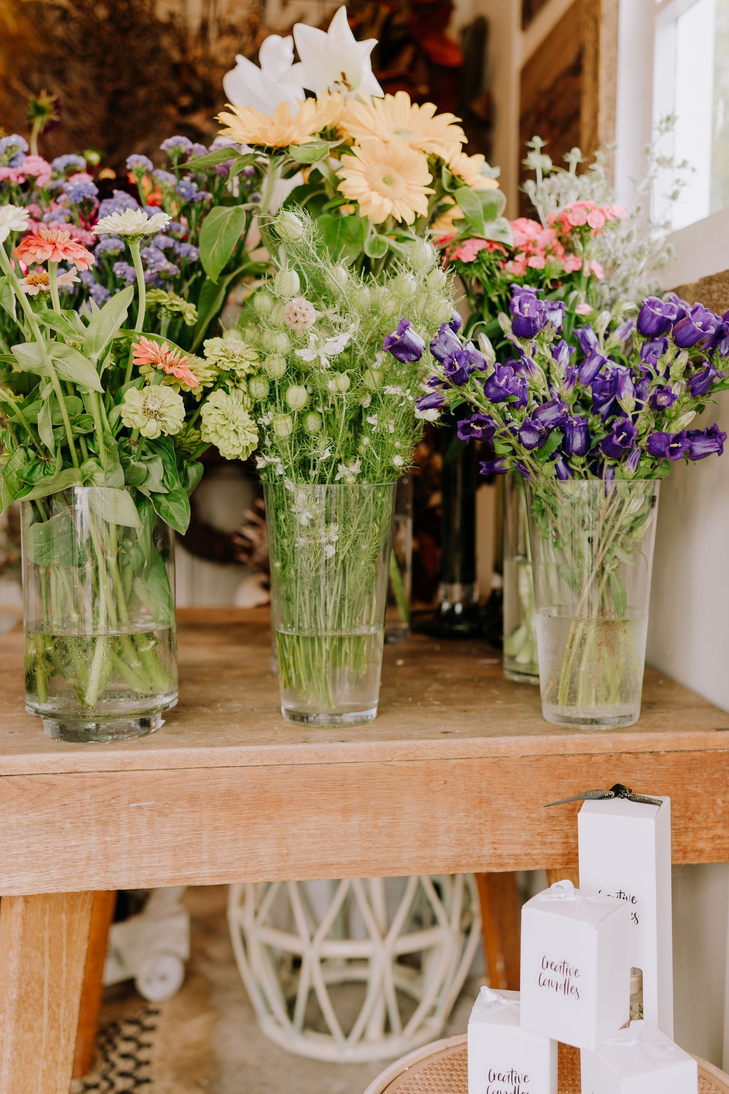 Colorful fresh flower arrangements in glass vases displayed on a wooden shelf.