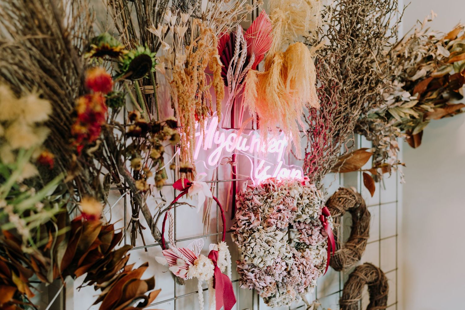Dried flowers and neon signage creating a bohemian wall display in a flower shop.