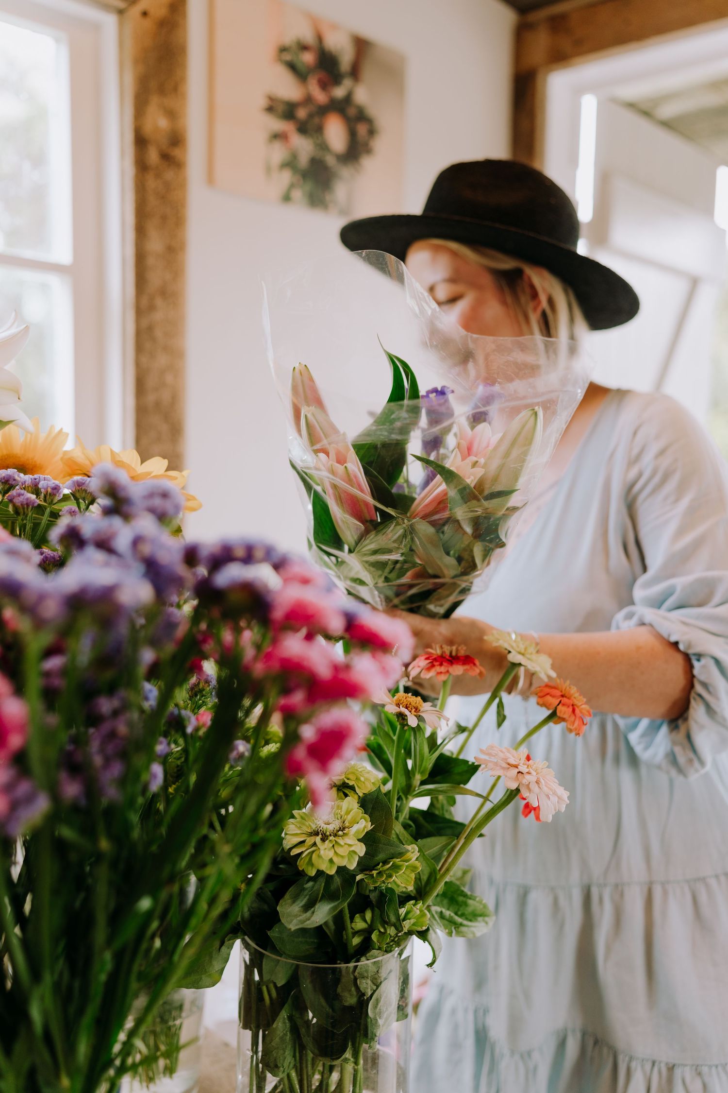 A florist in a white dress and black hat arranging fresh flowers in a bright studio.