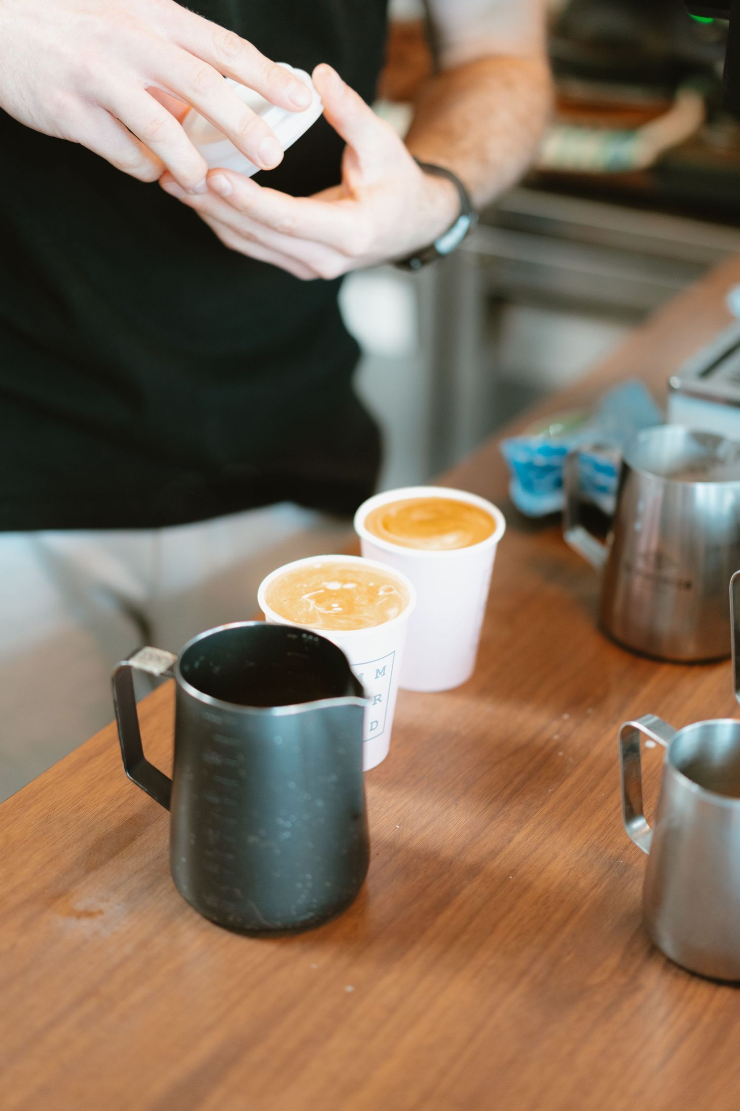 Barista preparing coffee drinks with milk pitchers and cups on wooden counter.
