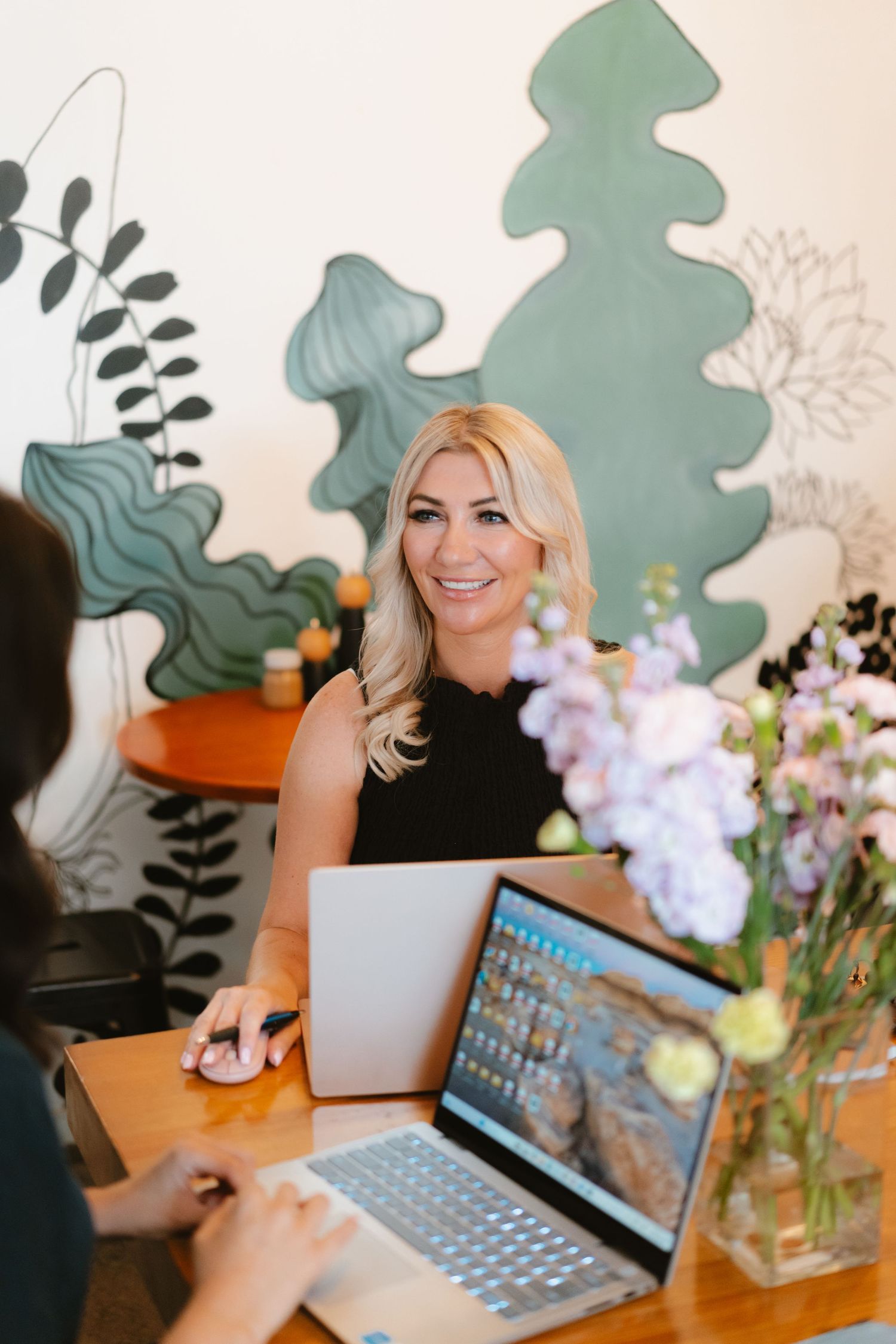 Modern office workspace with laptop, floral arrangement and decorative wall art.