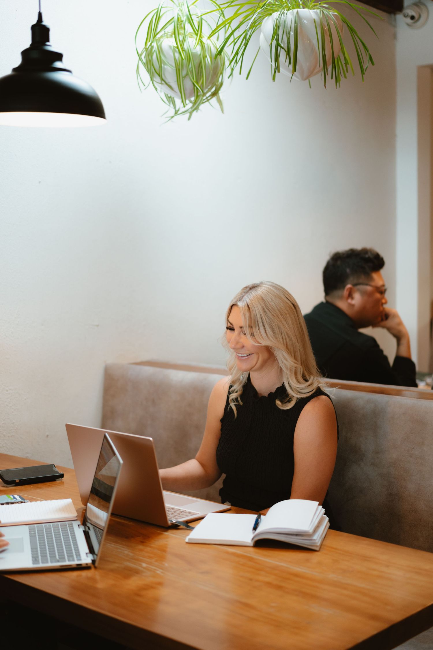Professional working on laptop in modern coffee shop setting with hanging plant.