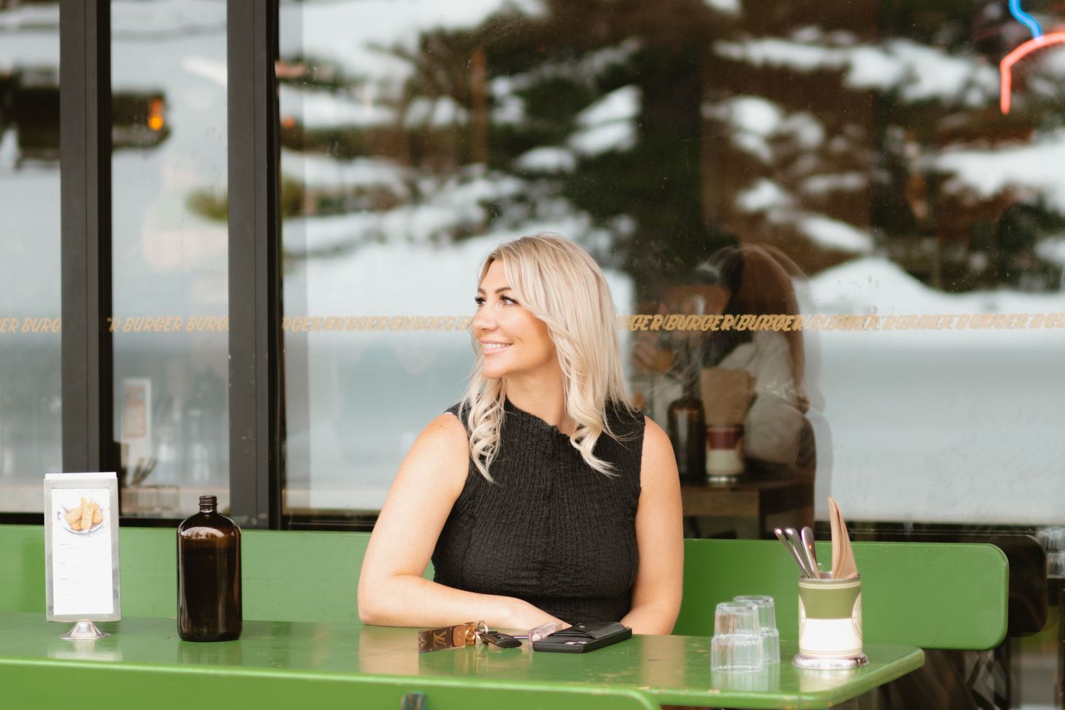 A woman sits at green counter in modern cafe with ocean view.