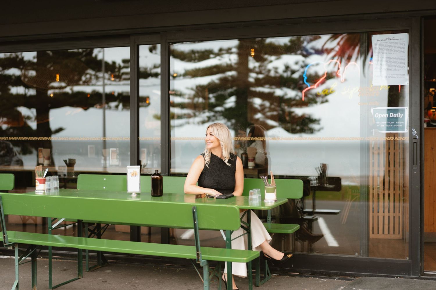 A woman in black sleeveless top relaxes at outdoor seating with green benches.