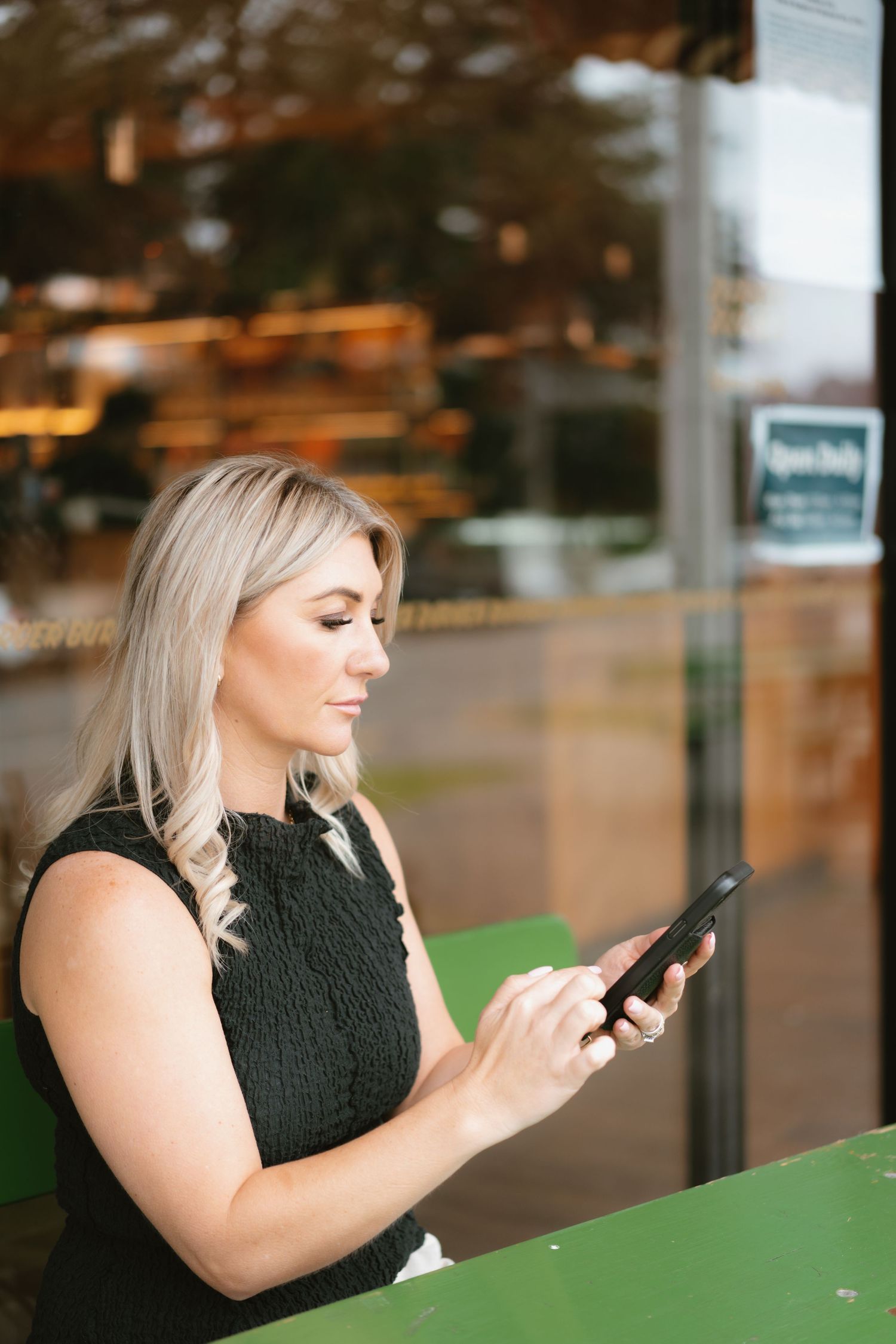 A woman in black top checks phone while seated at green counter.