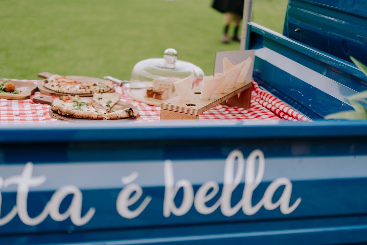 Food and drinks displayed on red checkered cloth on blue cart with Italian text.