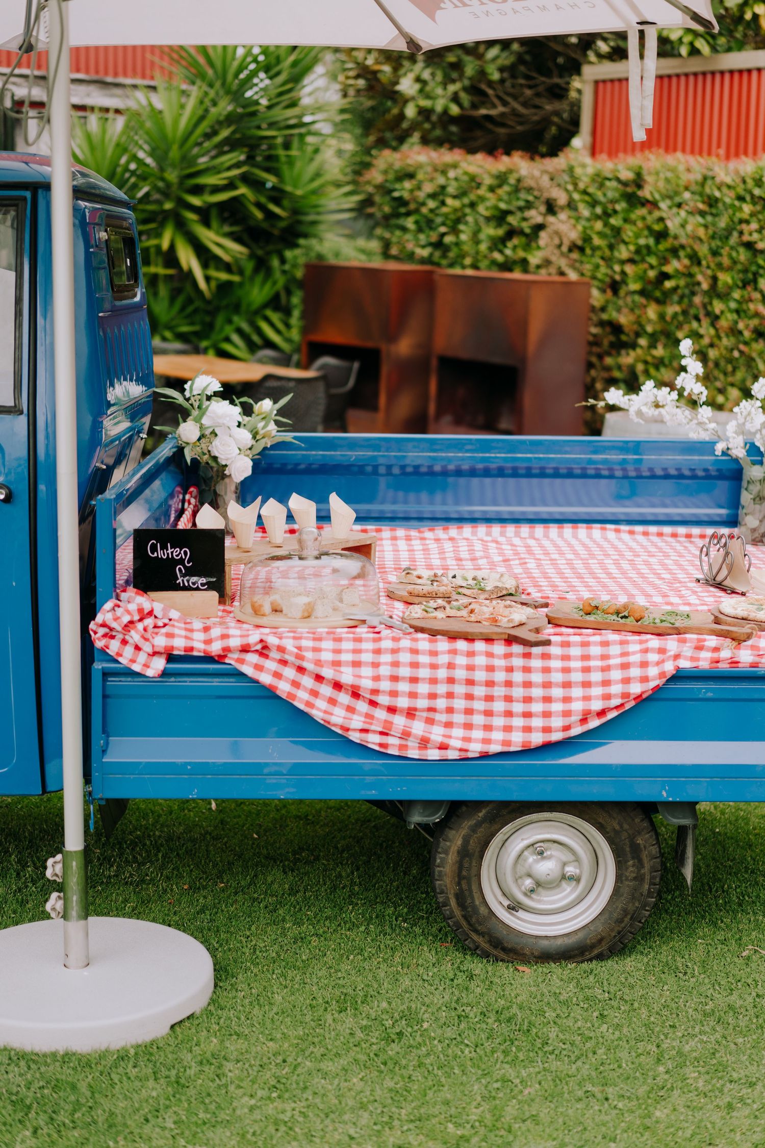 Blue vintage food cart with red checkered tablecloth and floral decorations on grass.