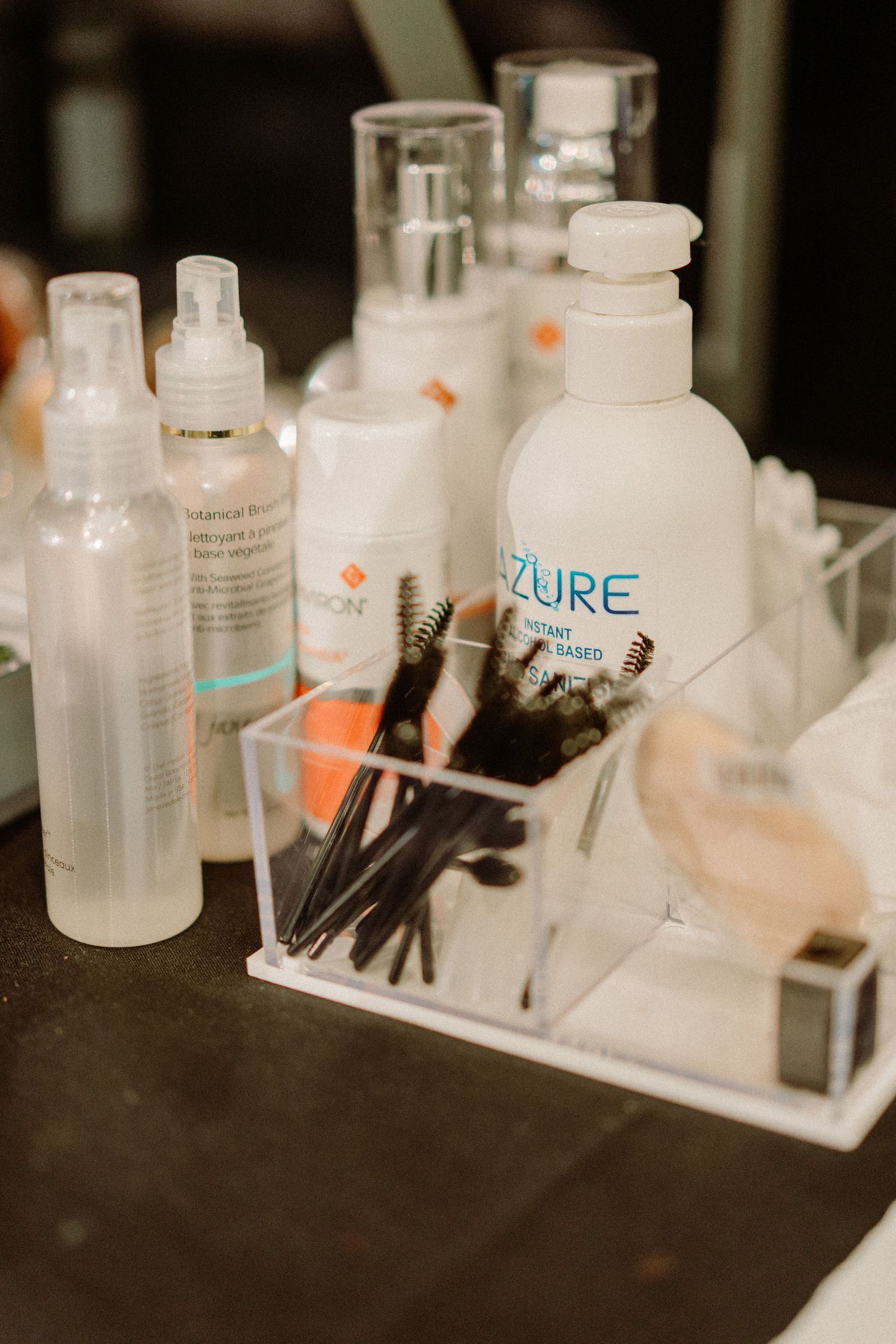Beauty products and makeup brushes arranged on a dark surface with skincare bottles and tools.