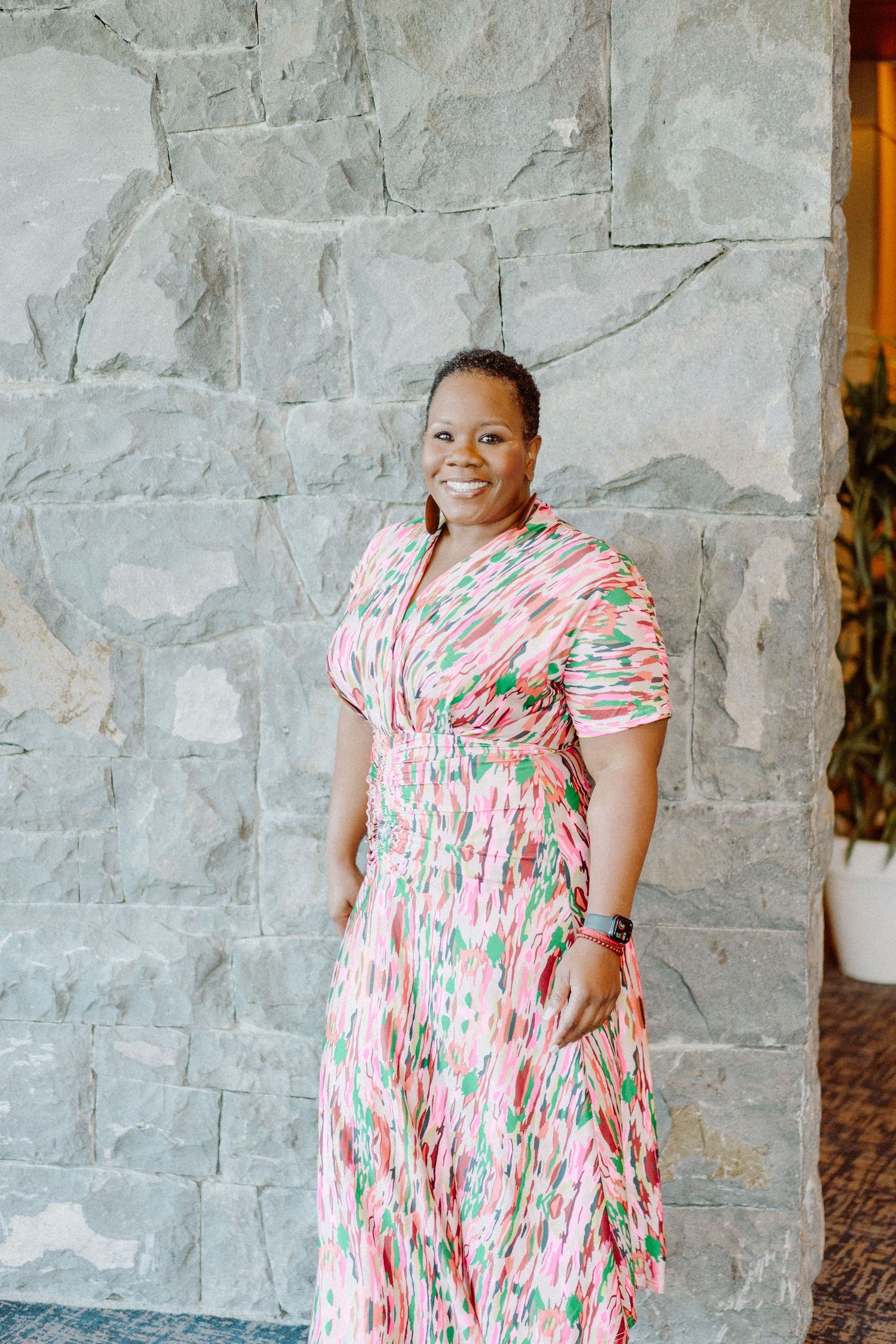 Portrait against stone wall wearing colorful floral print dress in professional setting.