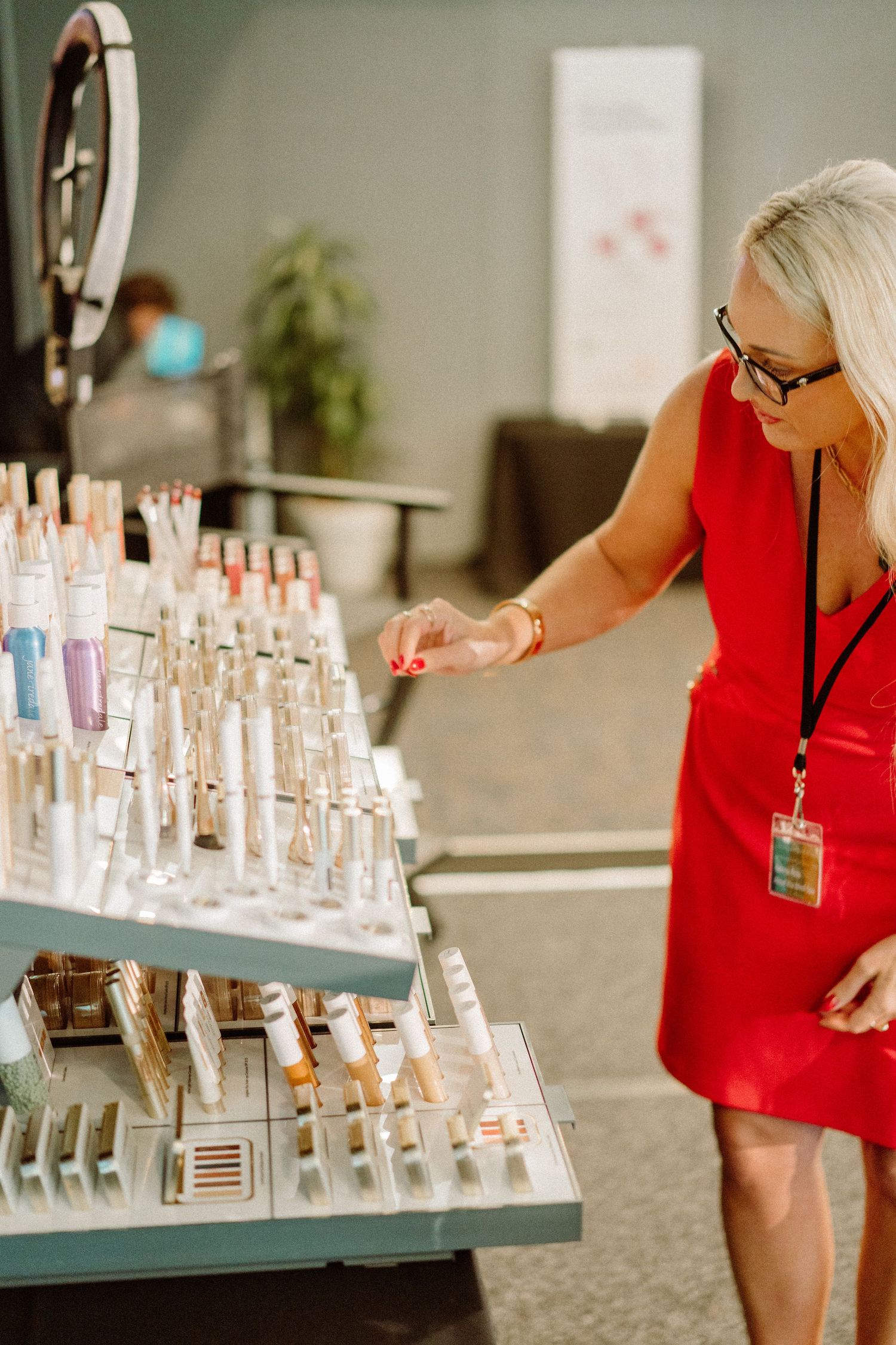 Woman in red dress examining beauty products displayed on tiered shelving.