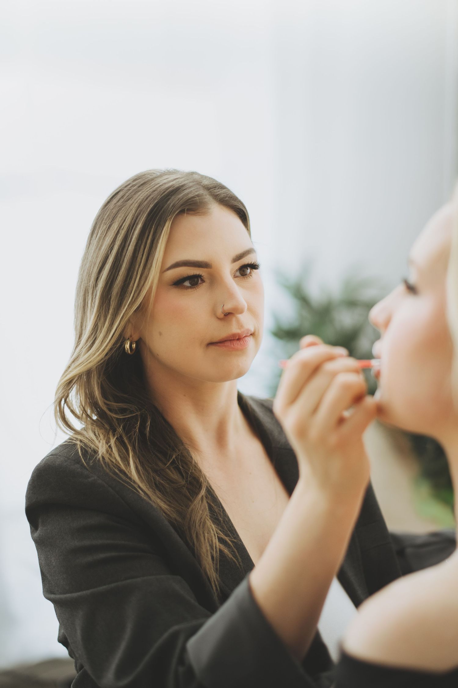 Professional makeup artist in black blazer carefully applying cosmetics to client during beauty session.