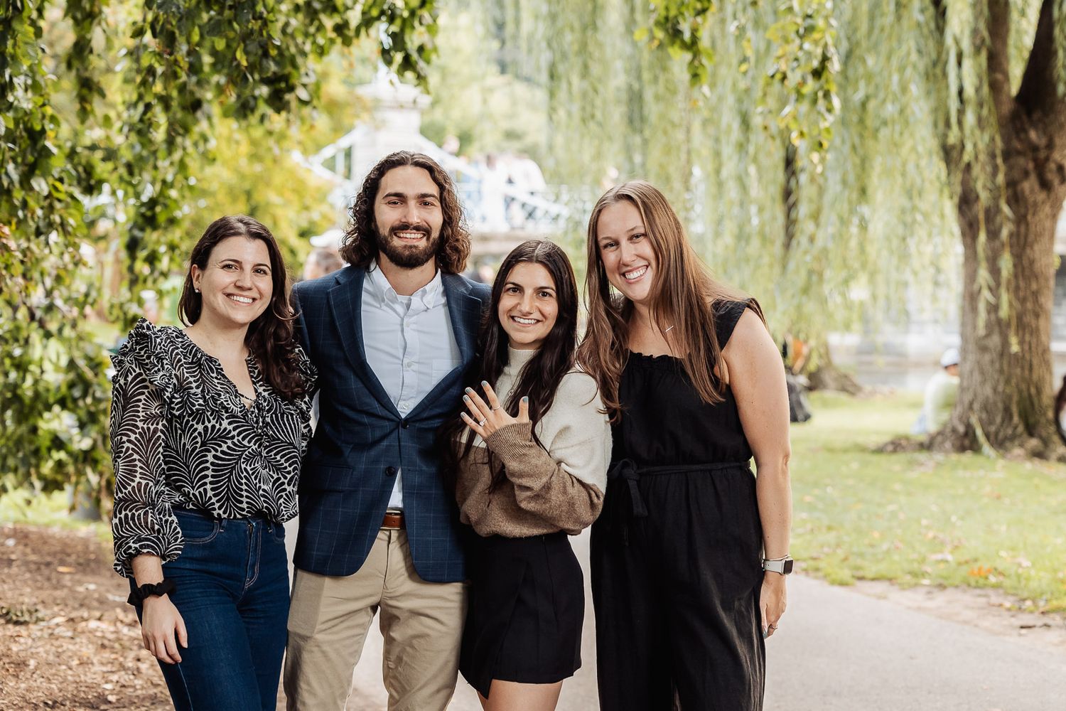 Group photo of friends posing together under willow trees in park.