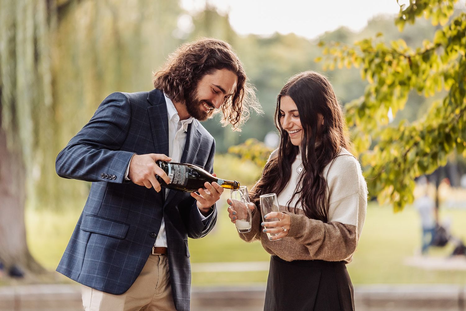 Couple pouring champagne to celebrate in park setting.