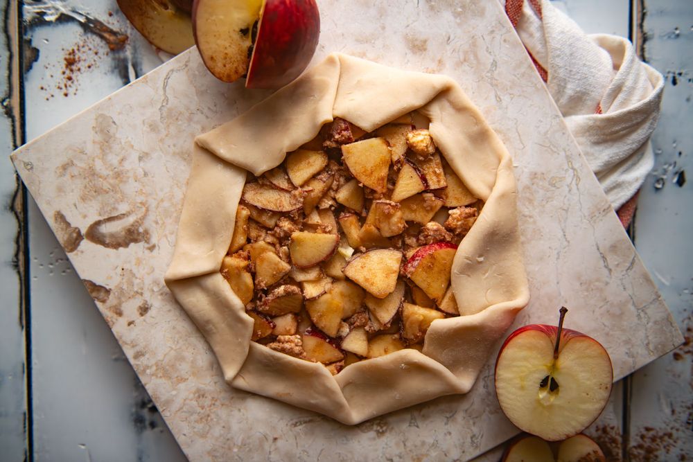Unbaked rustic apple galette with folded pastry edges and sliced apple filling.