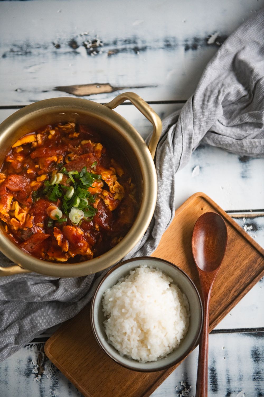 Spicy tomato stew served with steamed white rice in rustic bowls on white wooden surface.