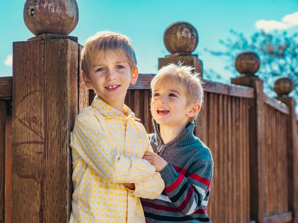 Two children laughing together while standing by wooden fence posts.
