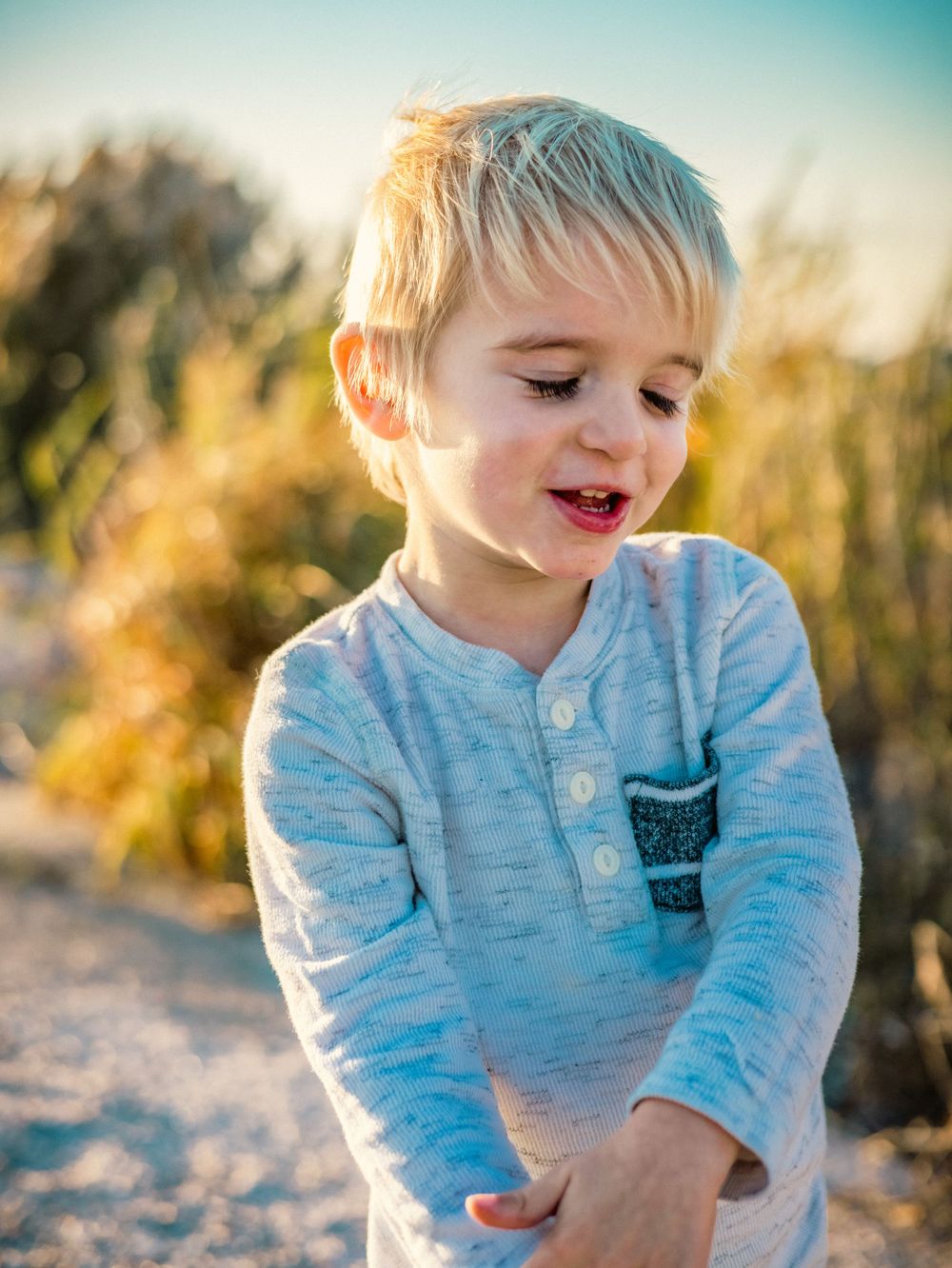 Child in light blue henley shirt looks down with a sweet expression.