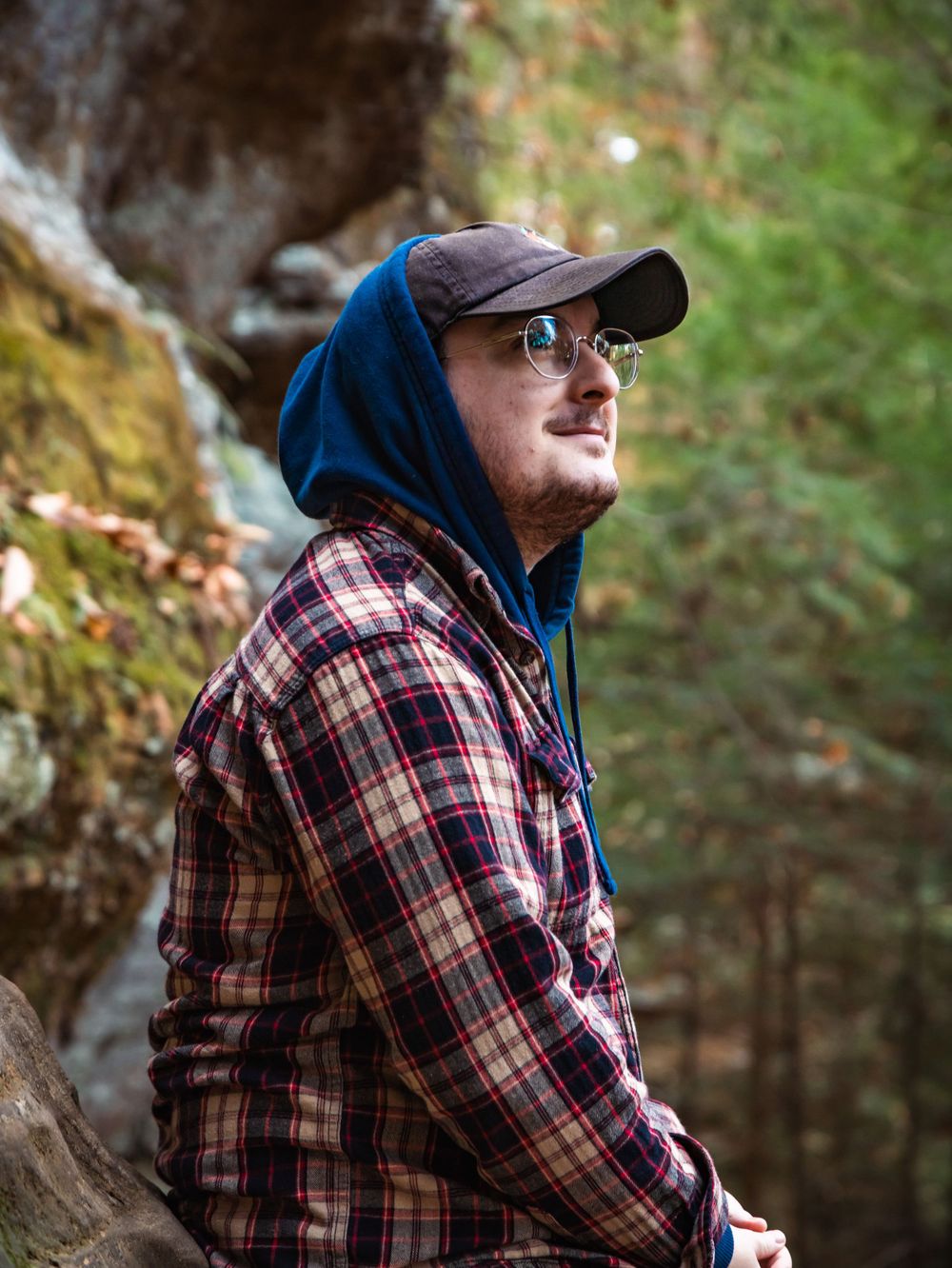 Explorer in plaid shirt and hoodie gazing at natural scenery while wearing a baseball cap.