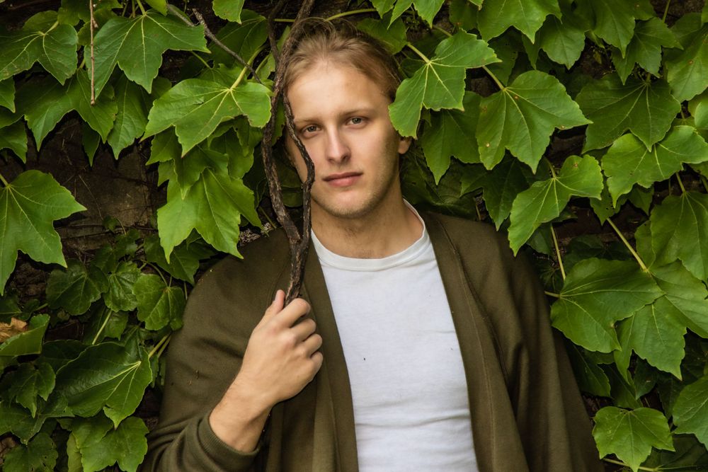 Portrait against green ivy backdrop wearing olive jacket.