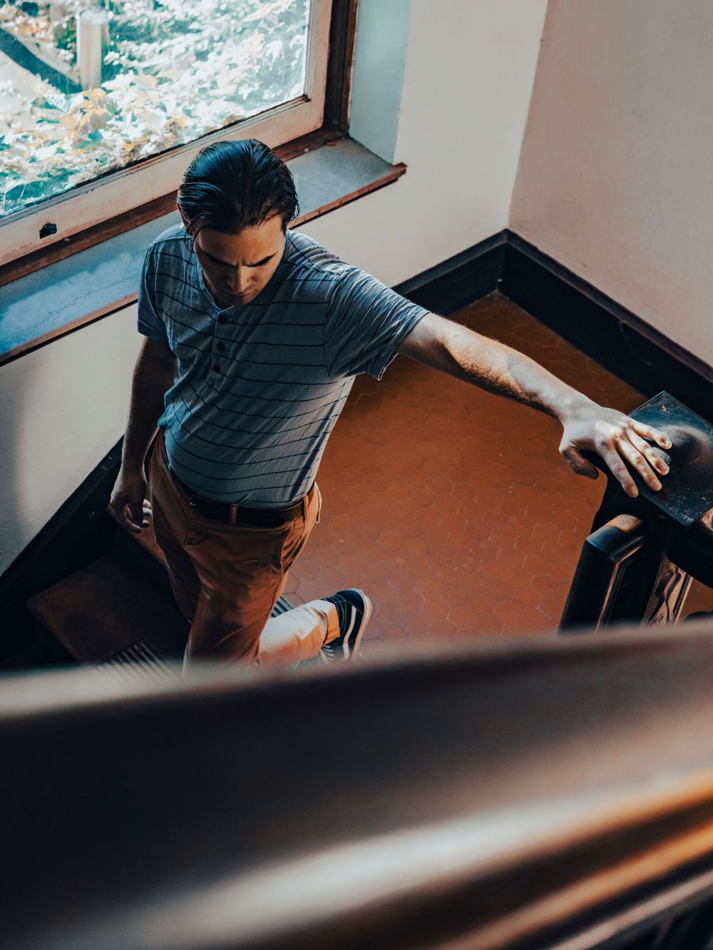 Person climbing stairs indoors seen from above wearing striped shirt and casual attire.