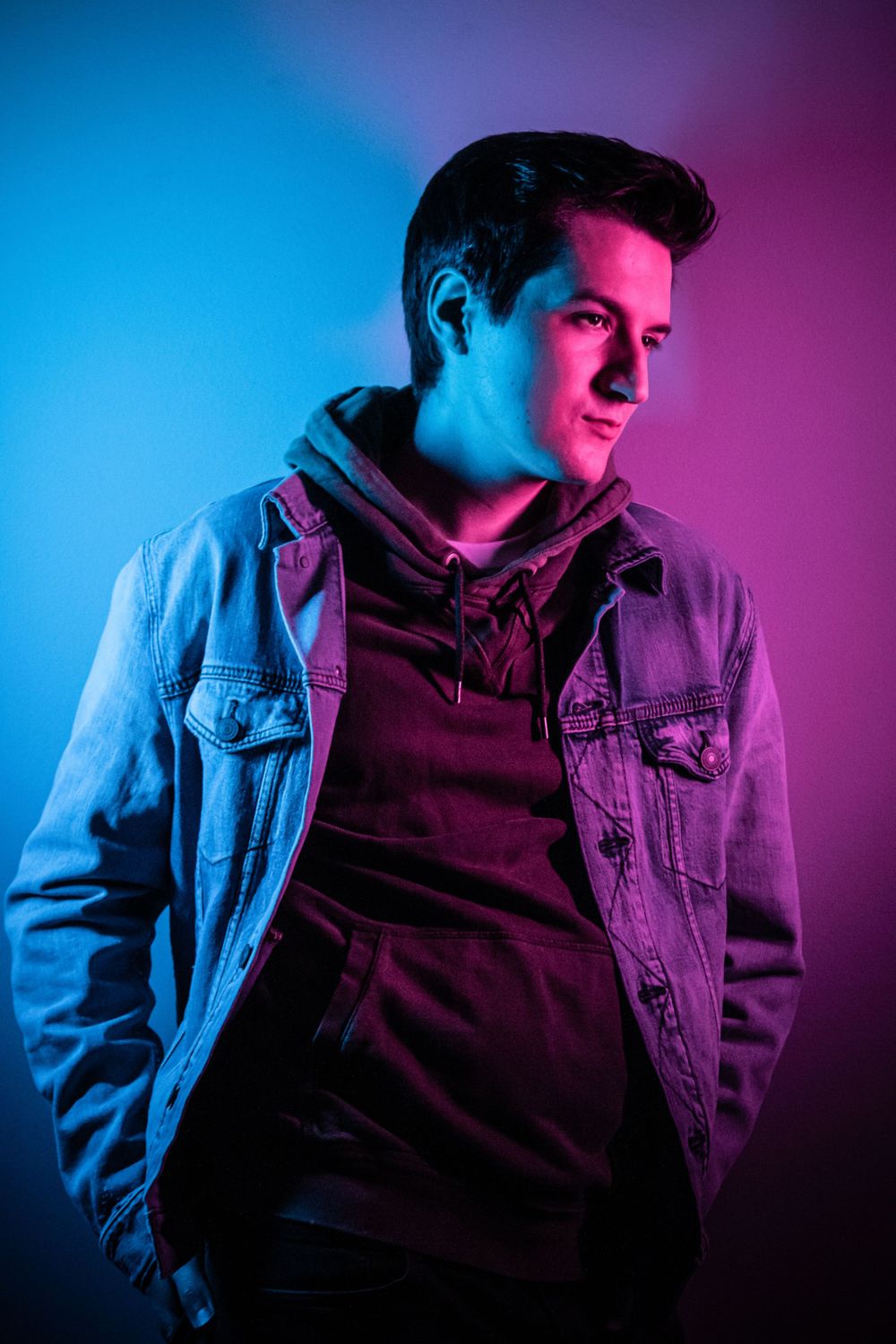 Portrait with neon lighting shows person in denim jacket against blue and pink backdrop.
