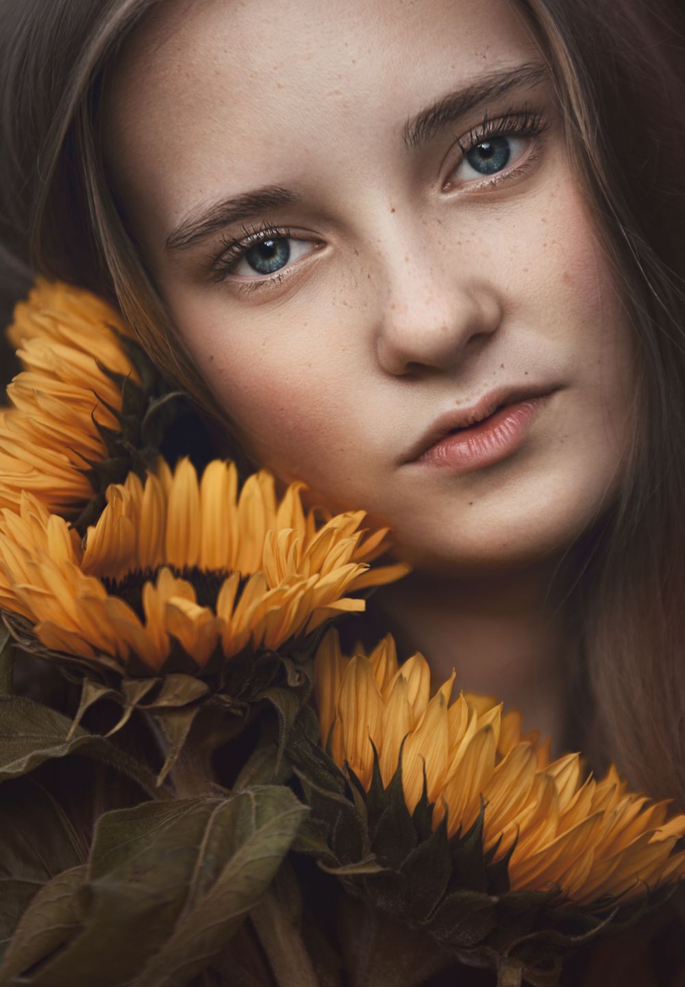 A close-up portrait with striking blue eyes and vibrant orange sunflowers creating a warm artistic composition.
