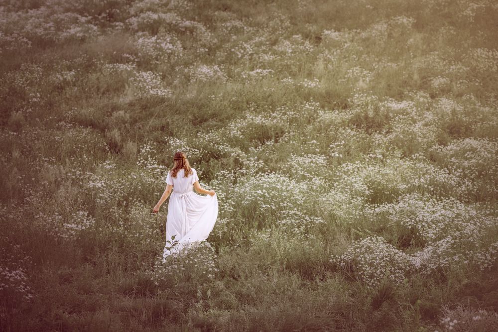 A person in a flowing white dress stands alone in a misty green field with a dreamy vintage aesthetic.