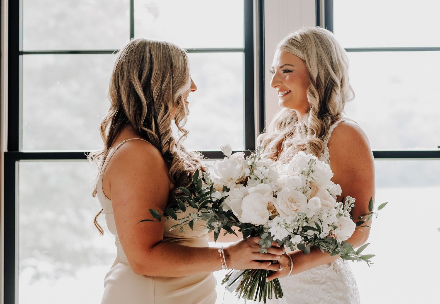 Two people sharing a joyful moment with a beautiful white floral bouquet in front of bright windows.