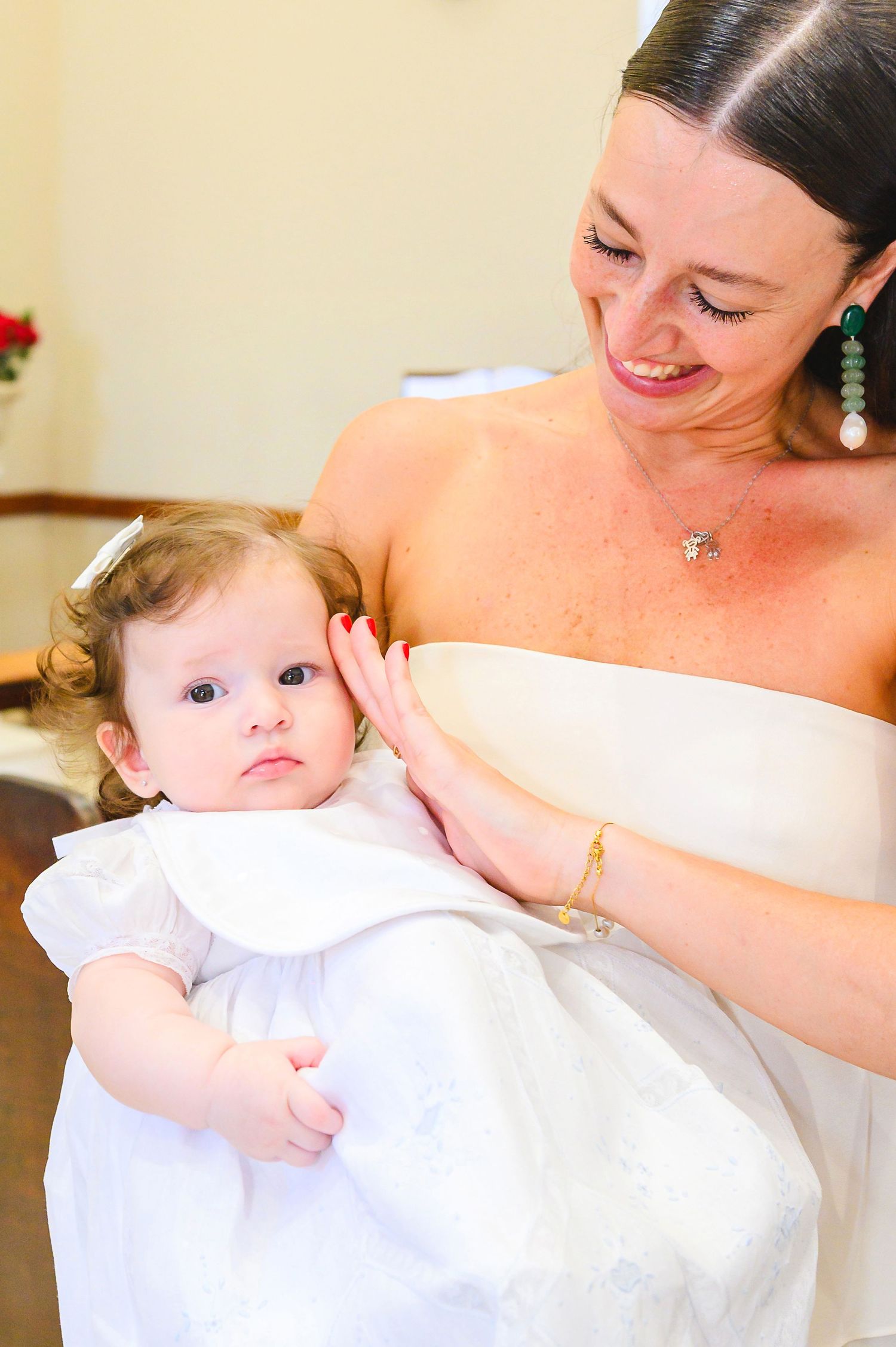 A tender moment captured at a formal event shows someone in white holding a baby dressed in a delicate white gown.