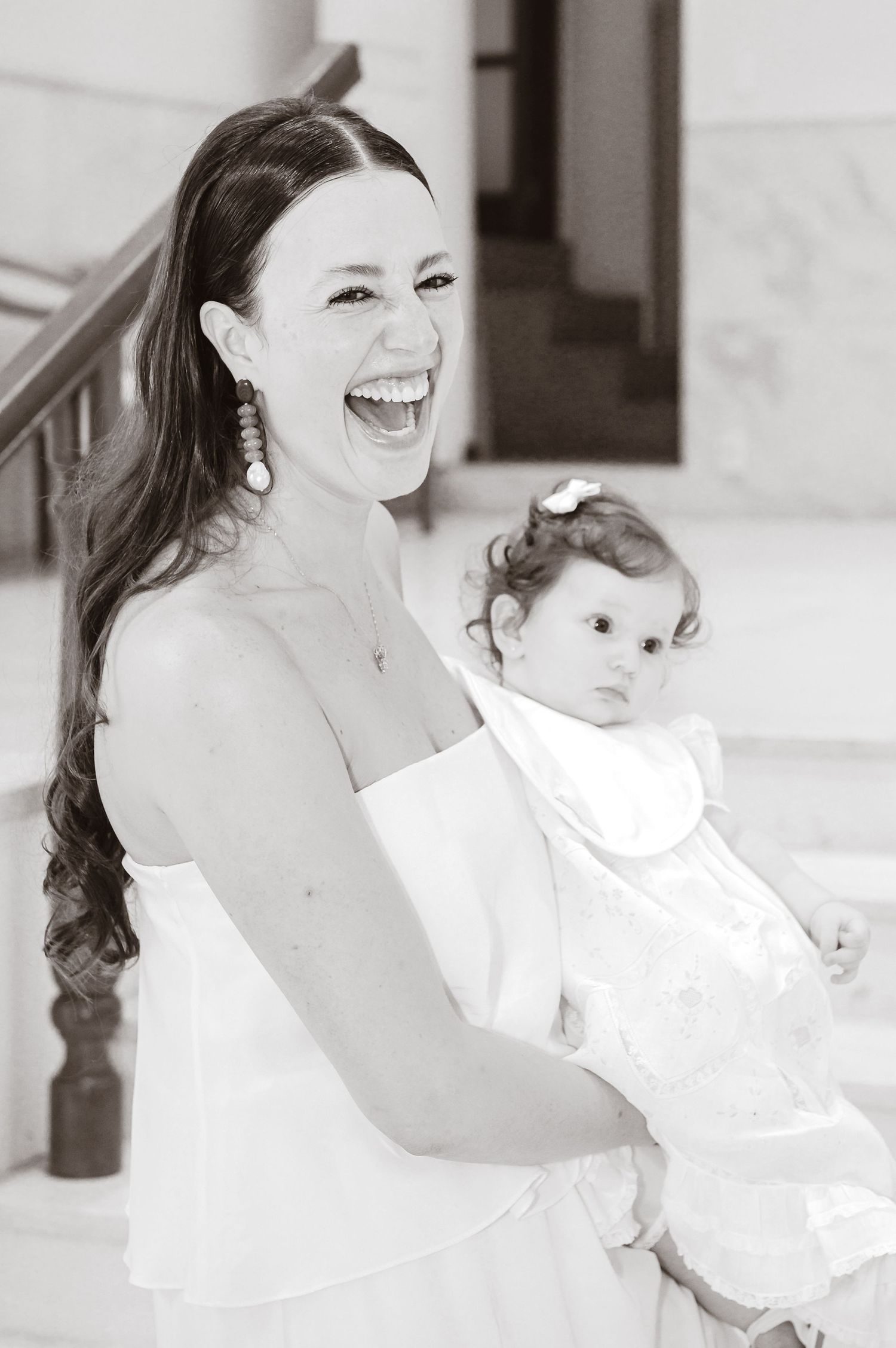 Black and white photo showing joyful expressions as a mother shares a tender moment with her baby in matching white outfits.