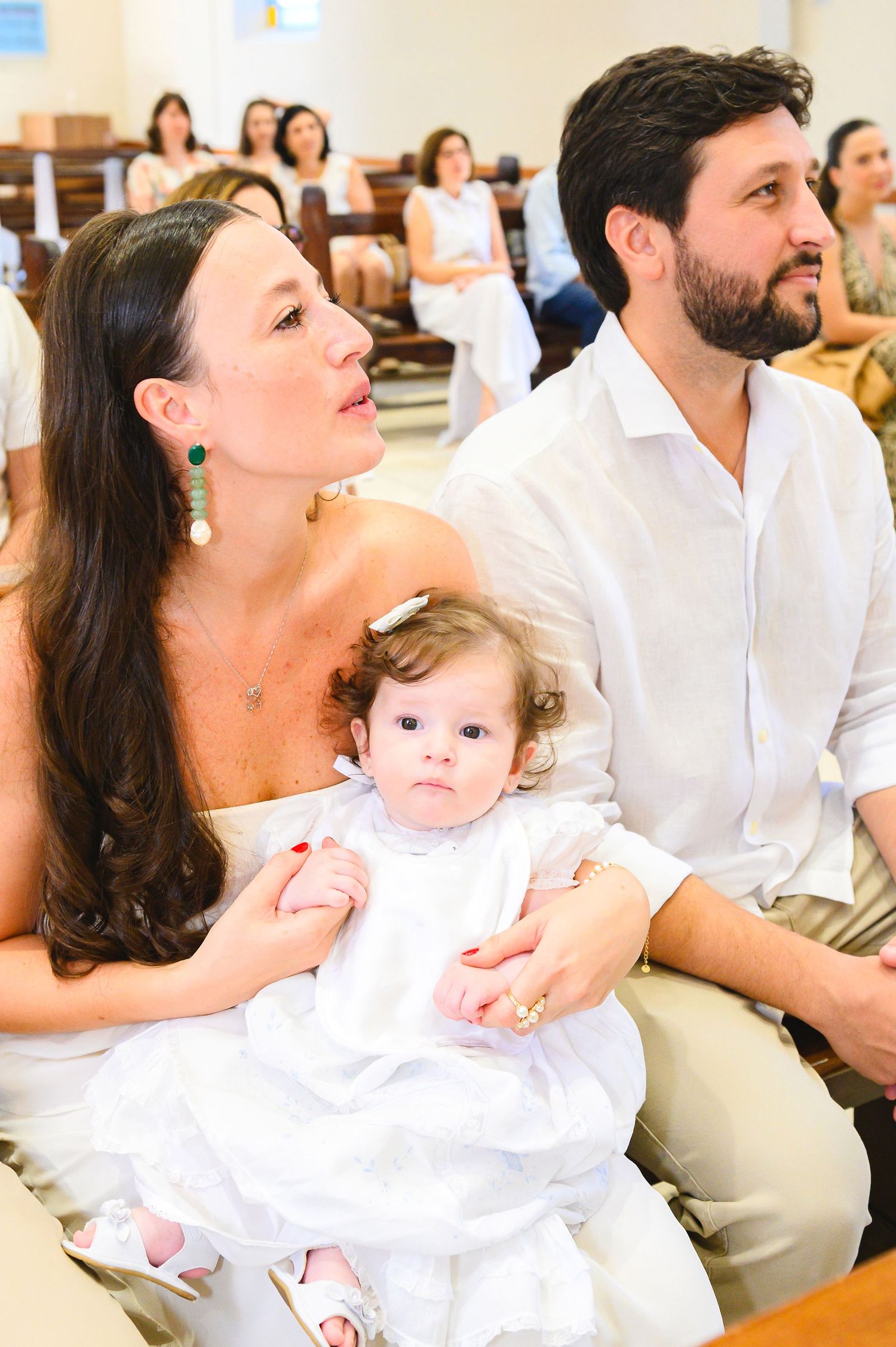 A family sits together during a special occasion in white attire with other guests visible in background rows.