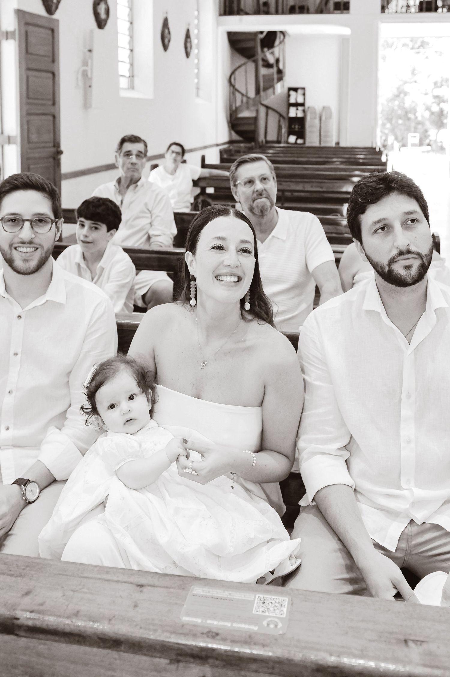 A group seated in wooden church pews during a special ceremony in a white interior space.
