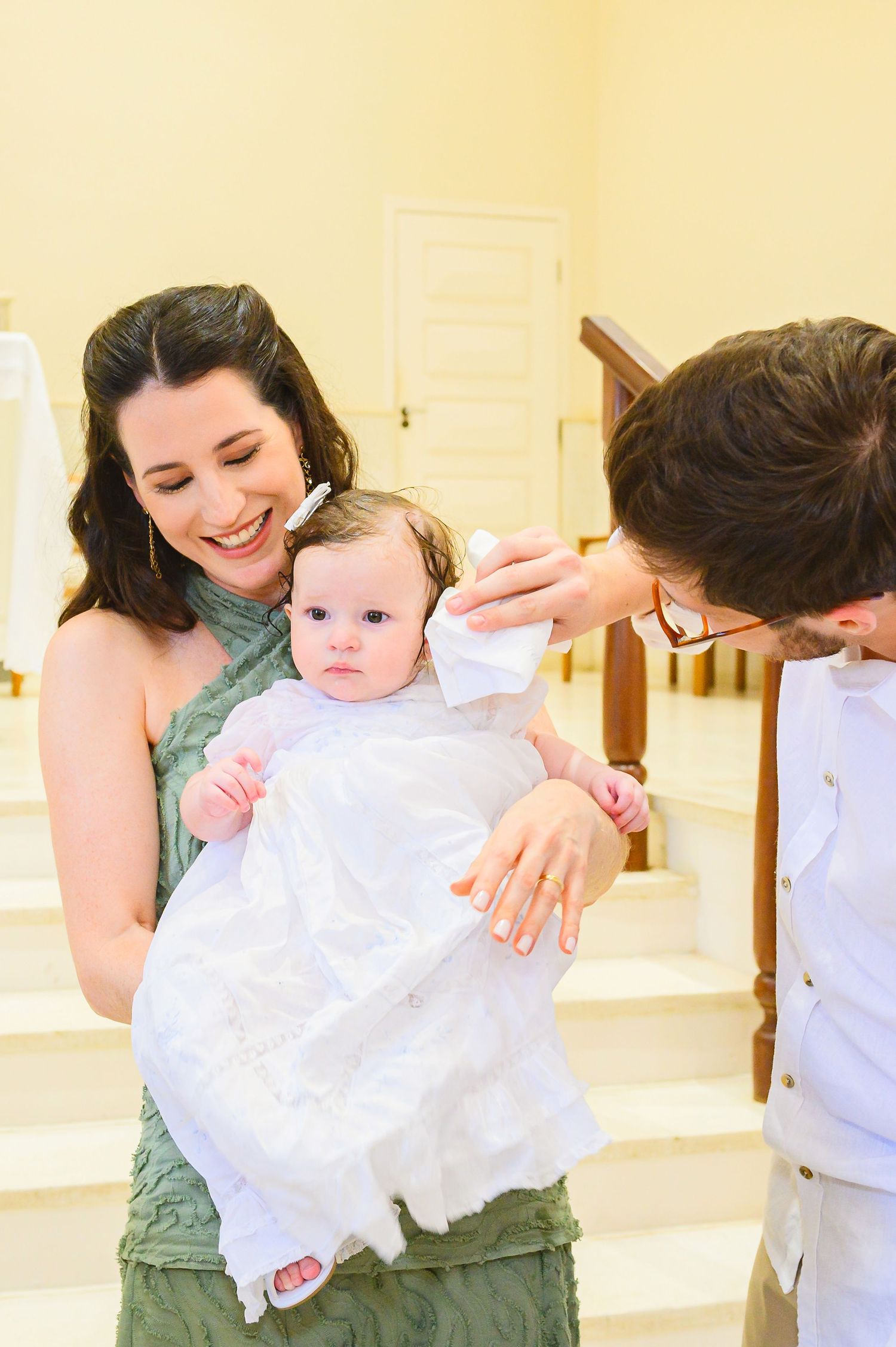 A small baby in a white christening gown being held while people gather around during a special ceremony.