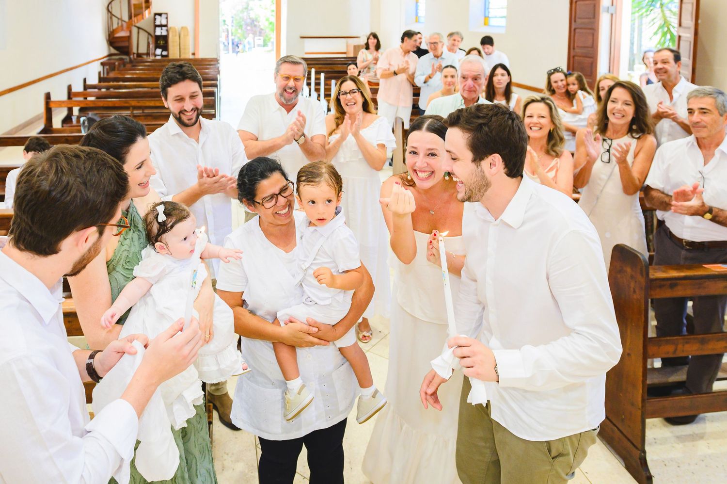 Wedding guests gather in a bright church interior, celebrating joyfully with clapping and smiles in white attire.