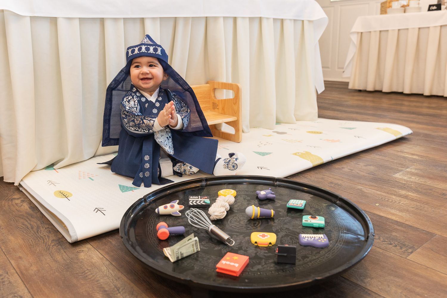 A child wearing navy blue sits on a floor with colorful toy blocks displayed on a black circular tray nearby.