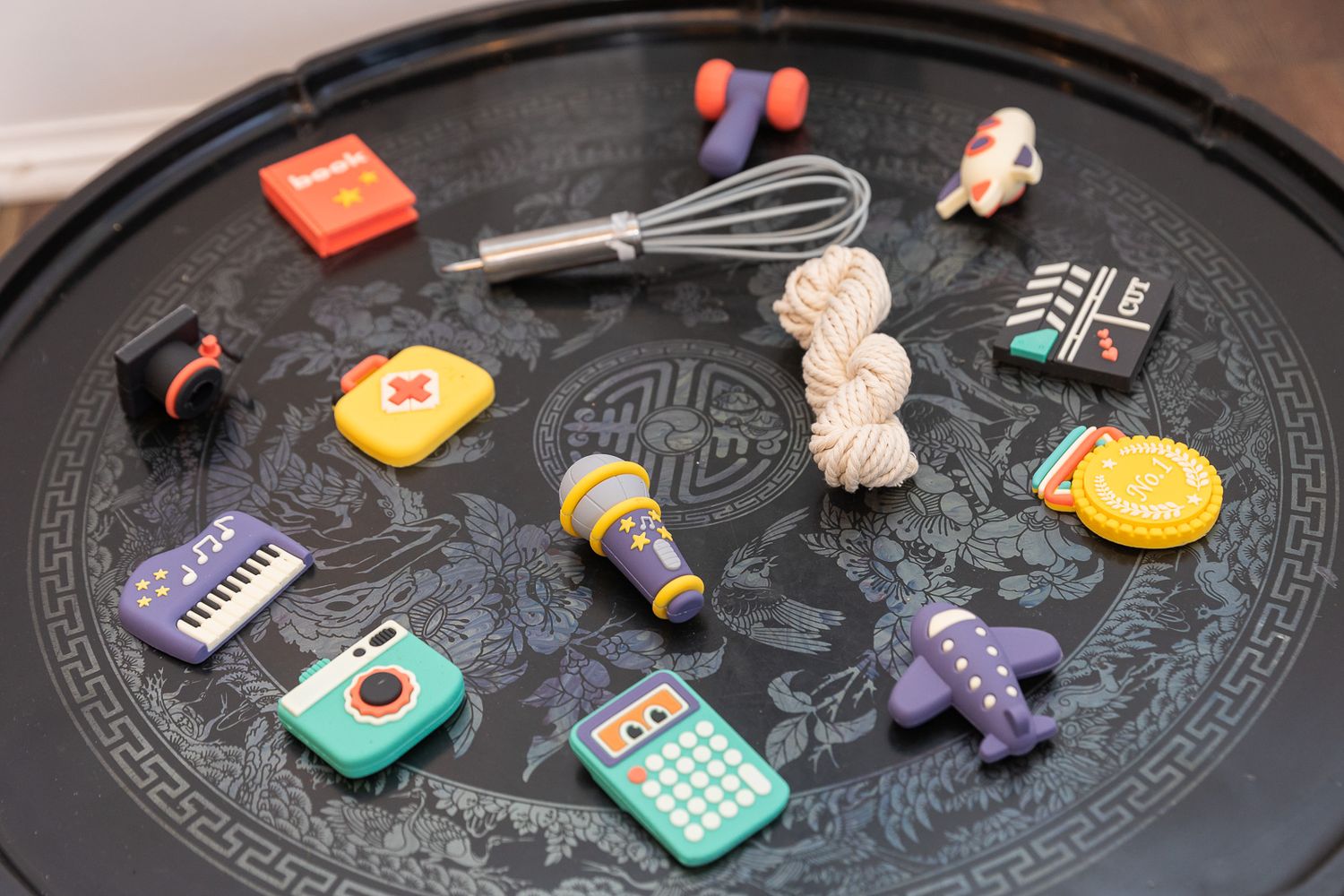 Colorful kitchen-themed fridge magnets and cooking utensils scattered on a dark circular surface.
