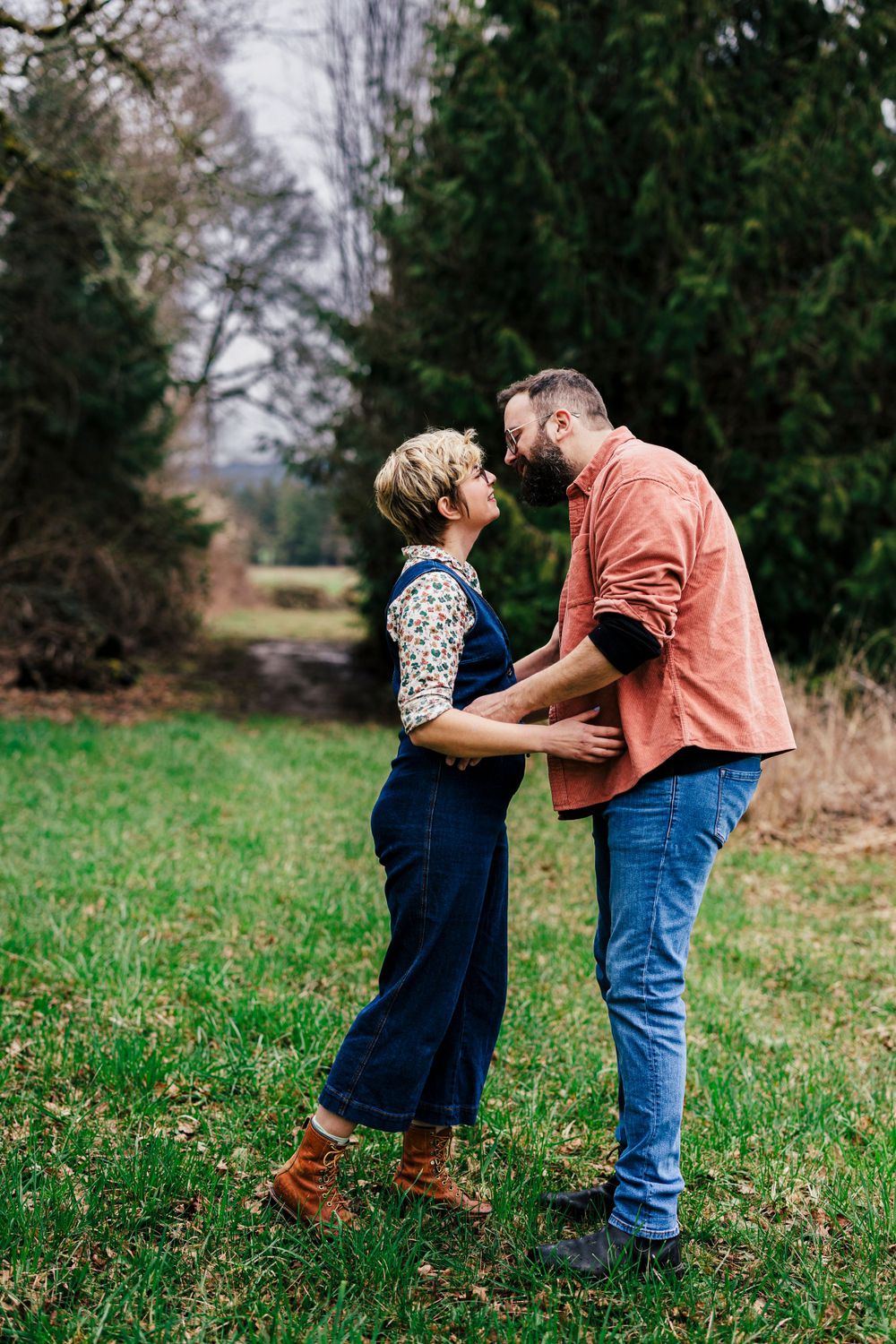A couple shares an intimate moment together while standing in a scenic outdoor setting with evergreen trees.