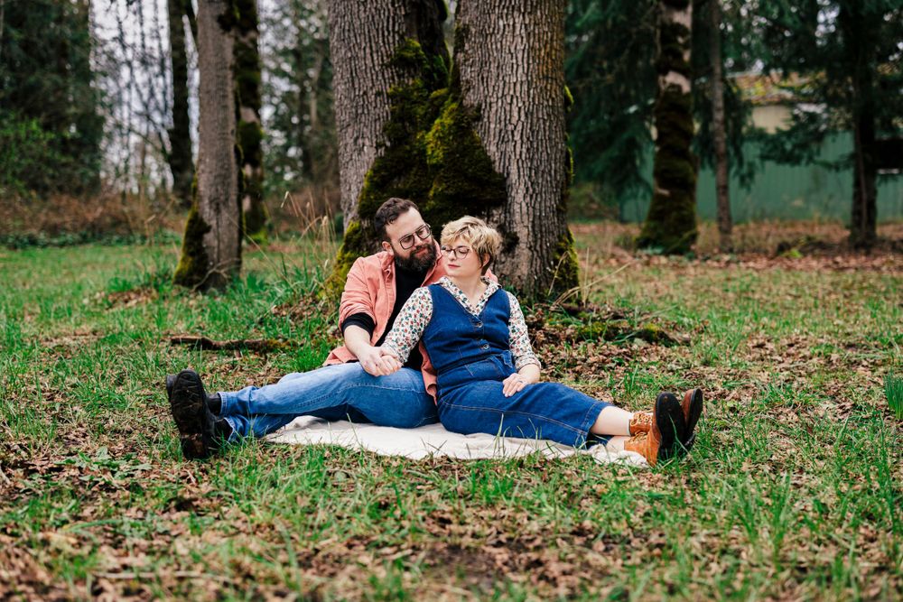 Two people share a romantic moment on a blanket in a wooded park setting during autumn.