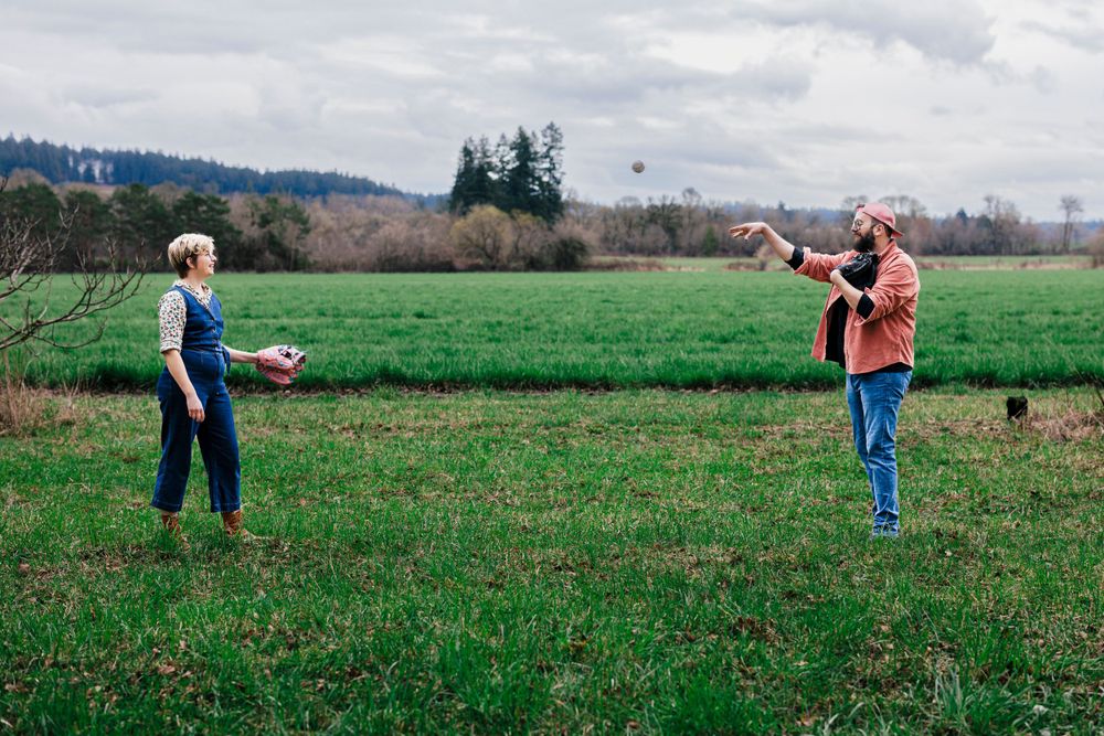 Two people stand in a green field playing catch with a ball on an overcast day.