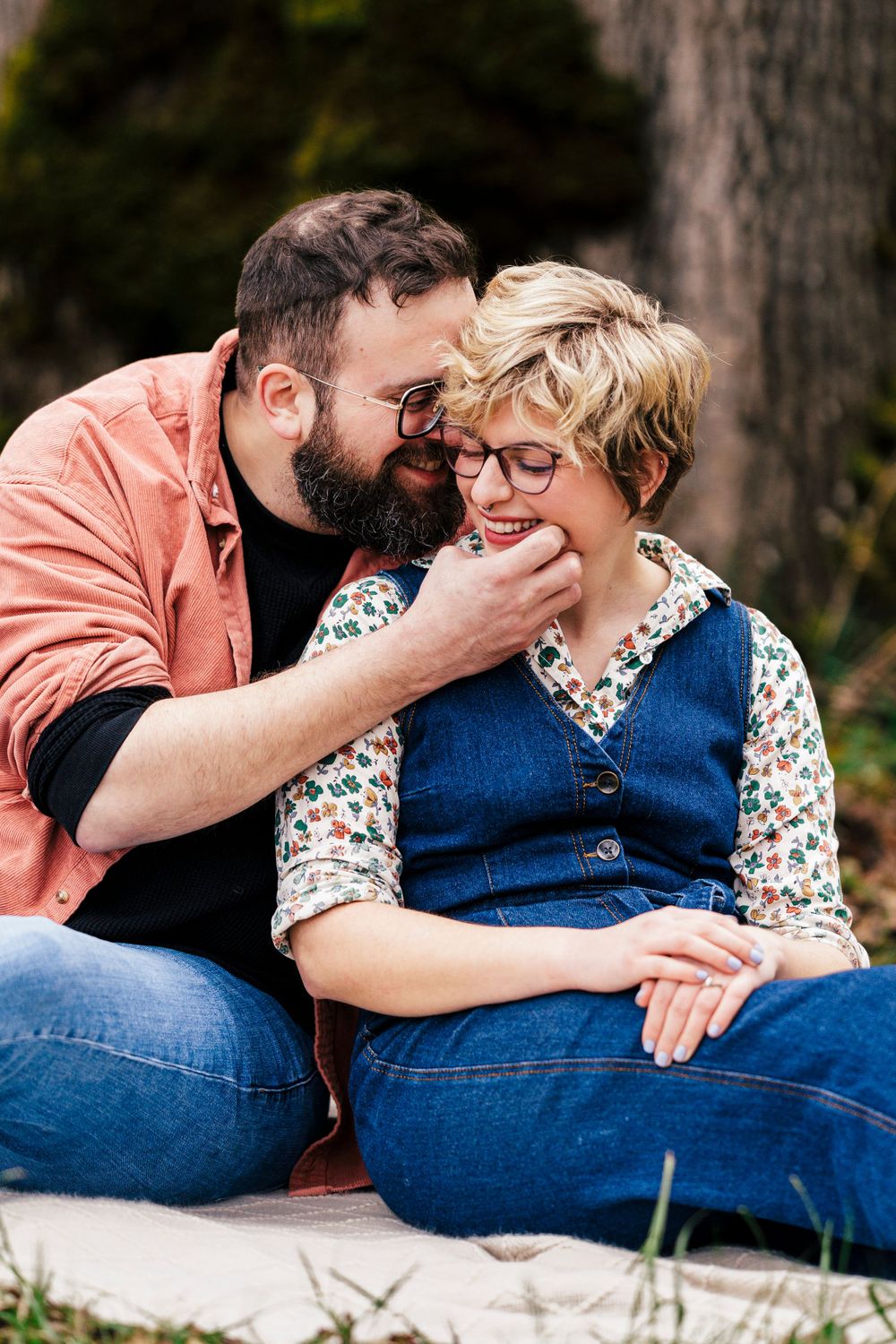 A romantic couple sitting together outdoors, sharing an intimate moment while wearing casual denim and fall attire.