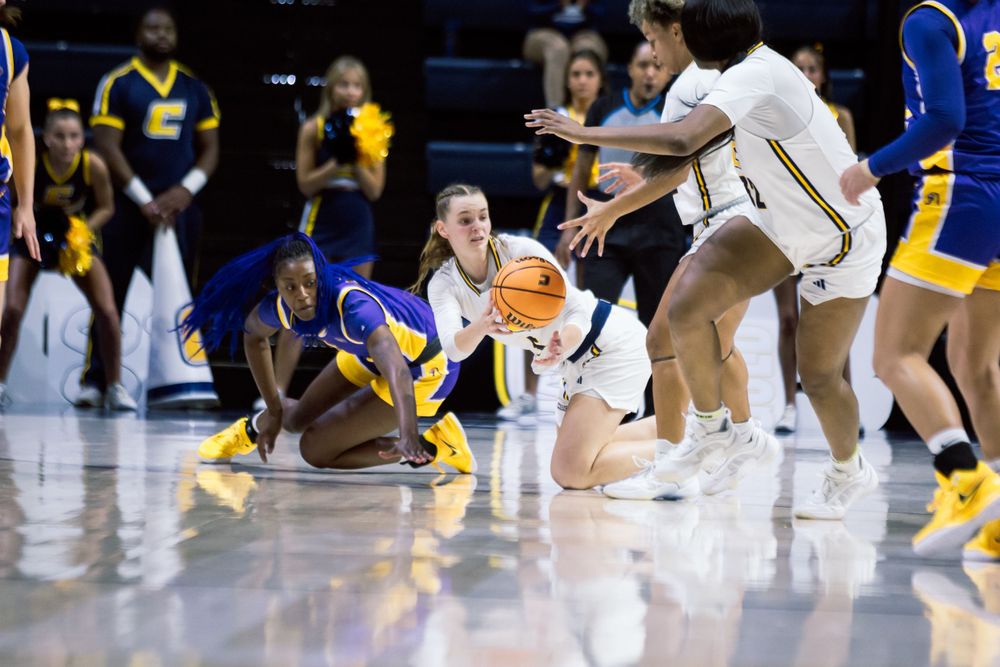 Basketball players dive for a loose ball during an intense game between two teams in blue and white uniforms.