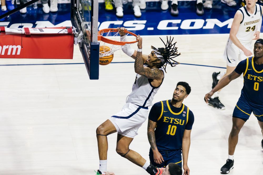 College basketball player drives to the hoop for a dunk attempt during an intense game action against defenders.