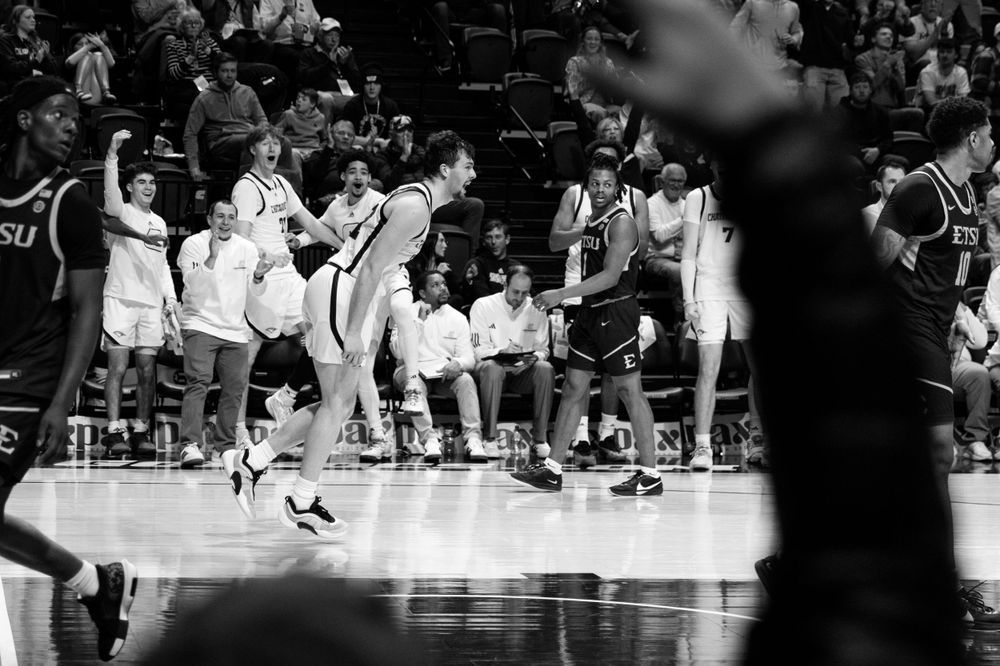 Black and white photo of basketball players celebrating on the sidelines during what appears to be a dramatic game moment.