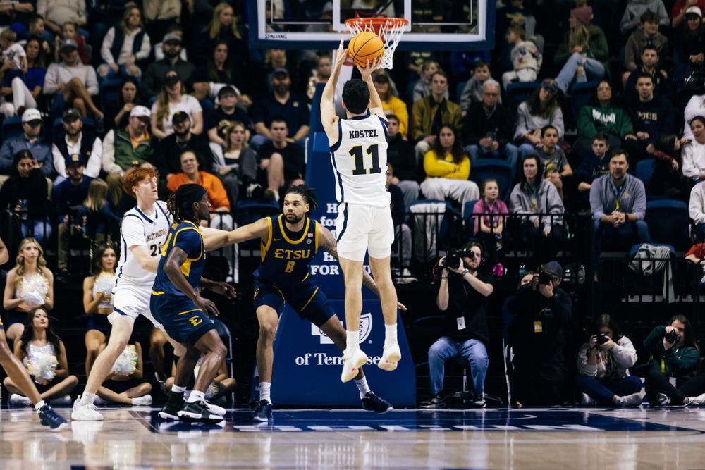 Basketball player in white jersey number 11 jumps high to shoot the ball during an intense game action.