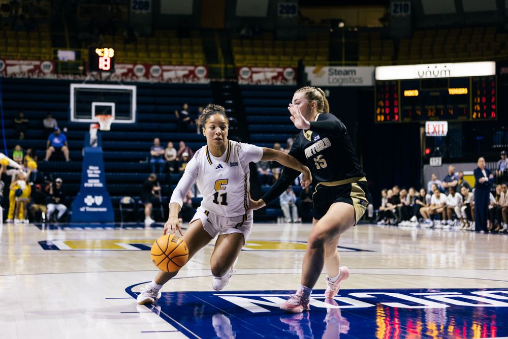 Basketball players compete for possession during an intense college basketball game on a blue court.