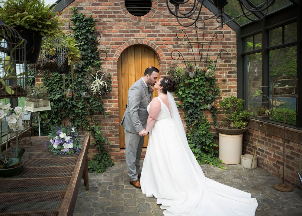 Wedding couple sharing a romantic moment by a rustic brick building with climbing vines.