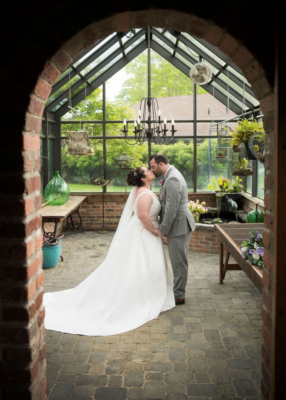 A couple share an intimate moment in a rustic greenhouse with brick archway and stone floor.