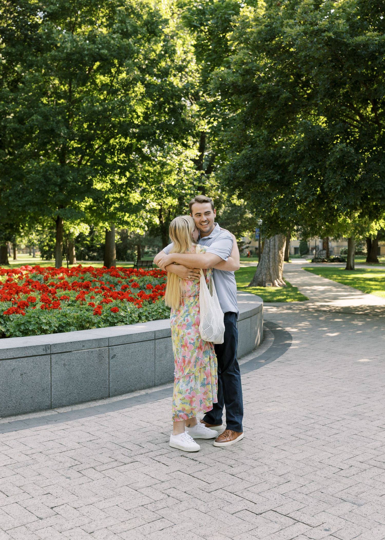 A tender moment captured between two people near a flower garden with brick pathways.